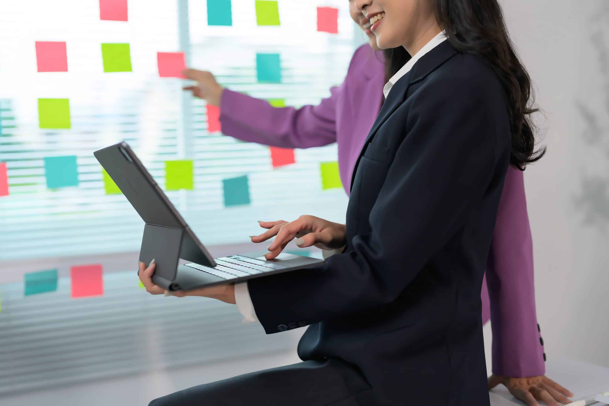 Two business professionals collaborating with a tablet and sticky notes in a modern office.